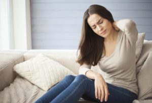 girl sitting on the couch at home with a headache and back pain.