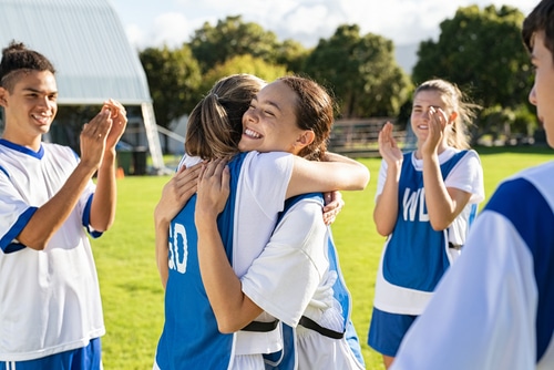 Soccer teammates embracing while players clapping hands on victory.